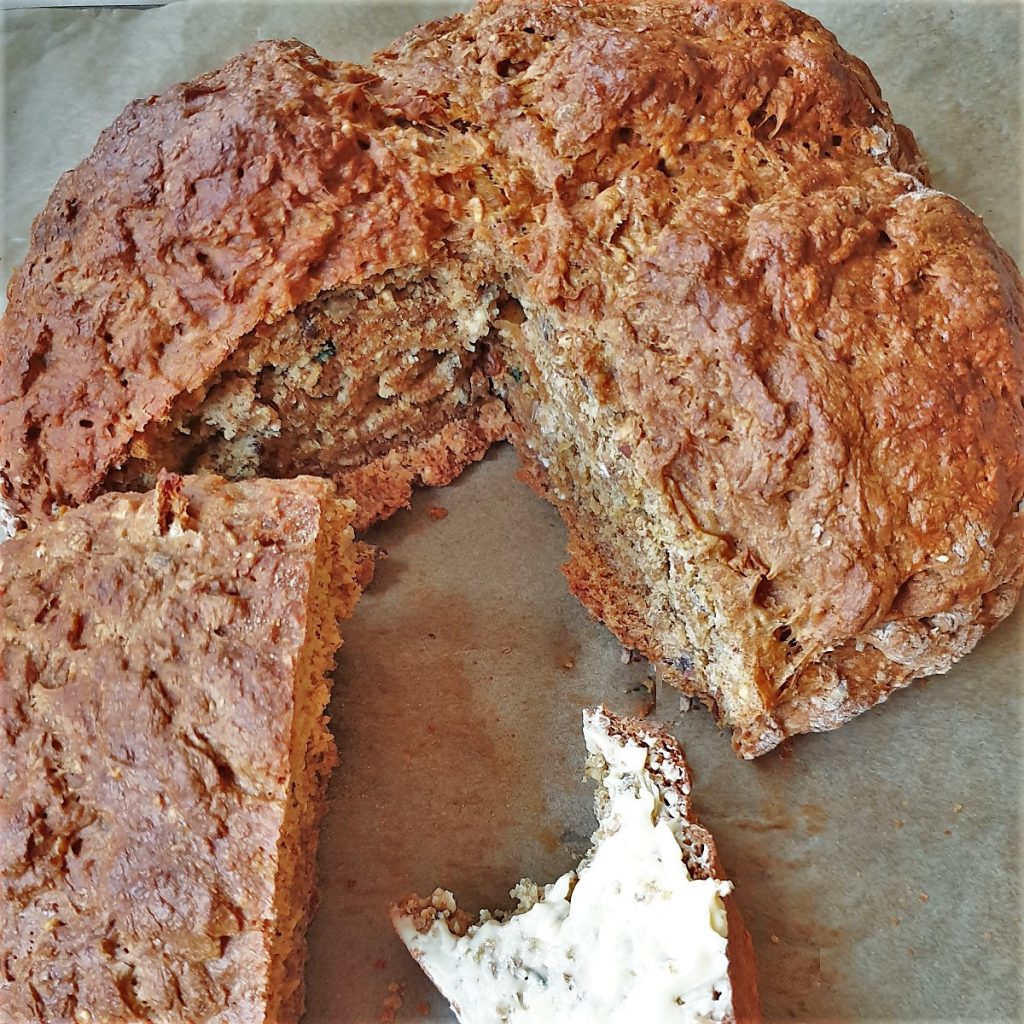 A loaf of wholemeal bread with a slice cut out and covered with butter.