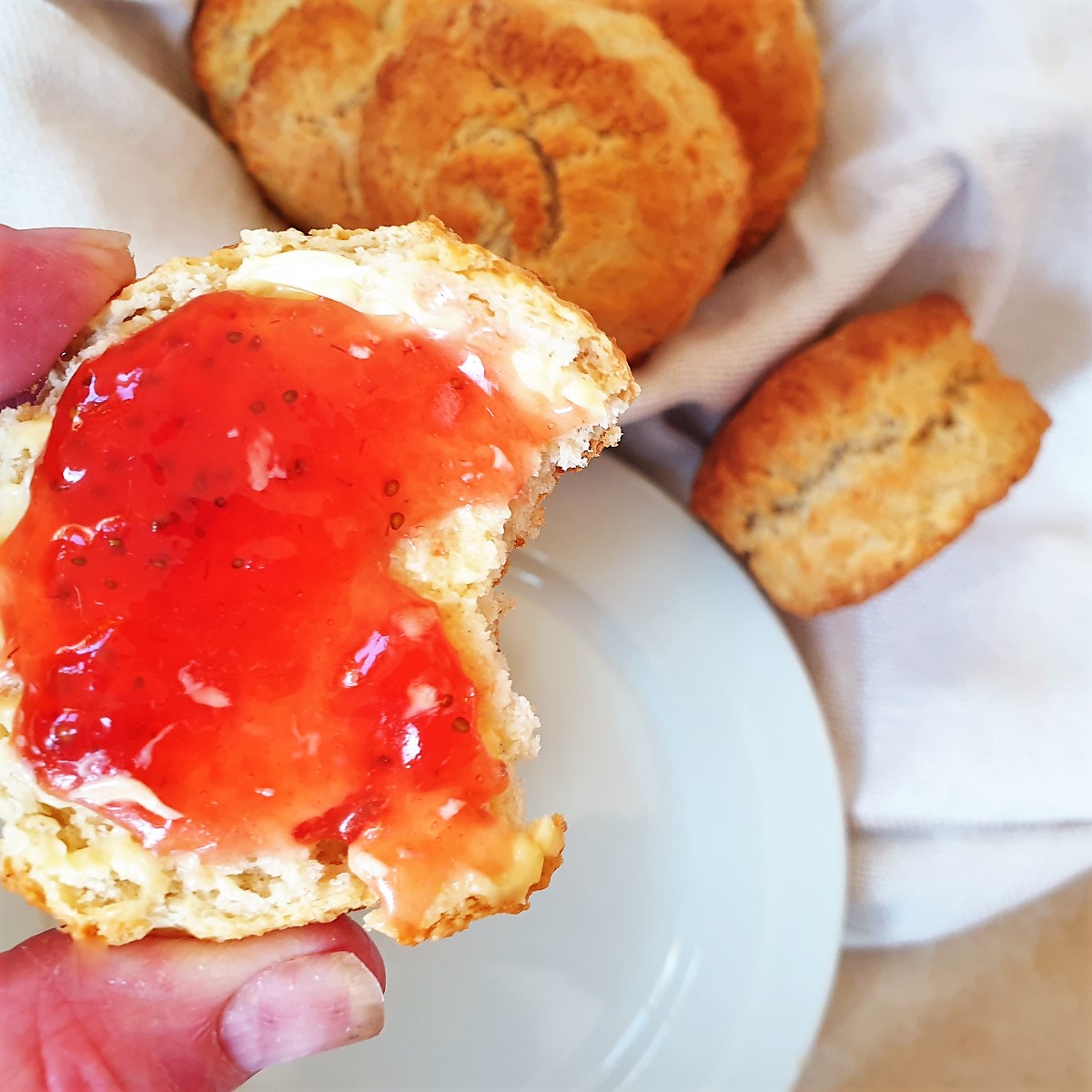 A scone covered in strawberry jam with a bite taken from it.