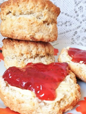 A scone covered in strawberry jam in front of a pile of scones.