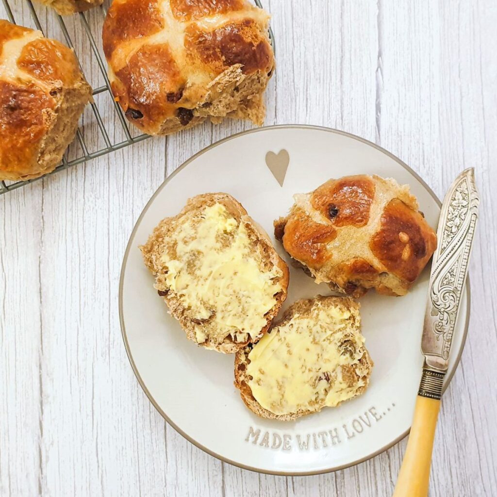 A buttered hot cross bun on a plate.