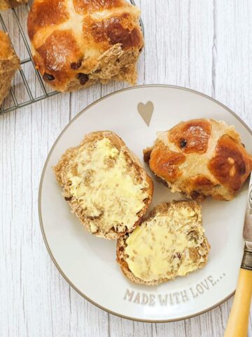 A buttered hot cross bun on a plate.