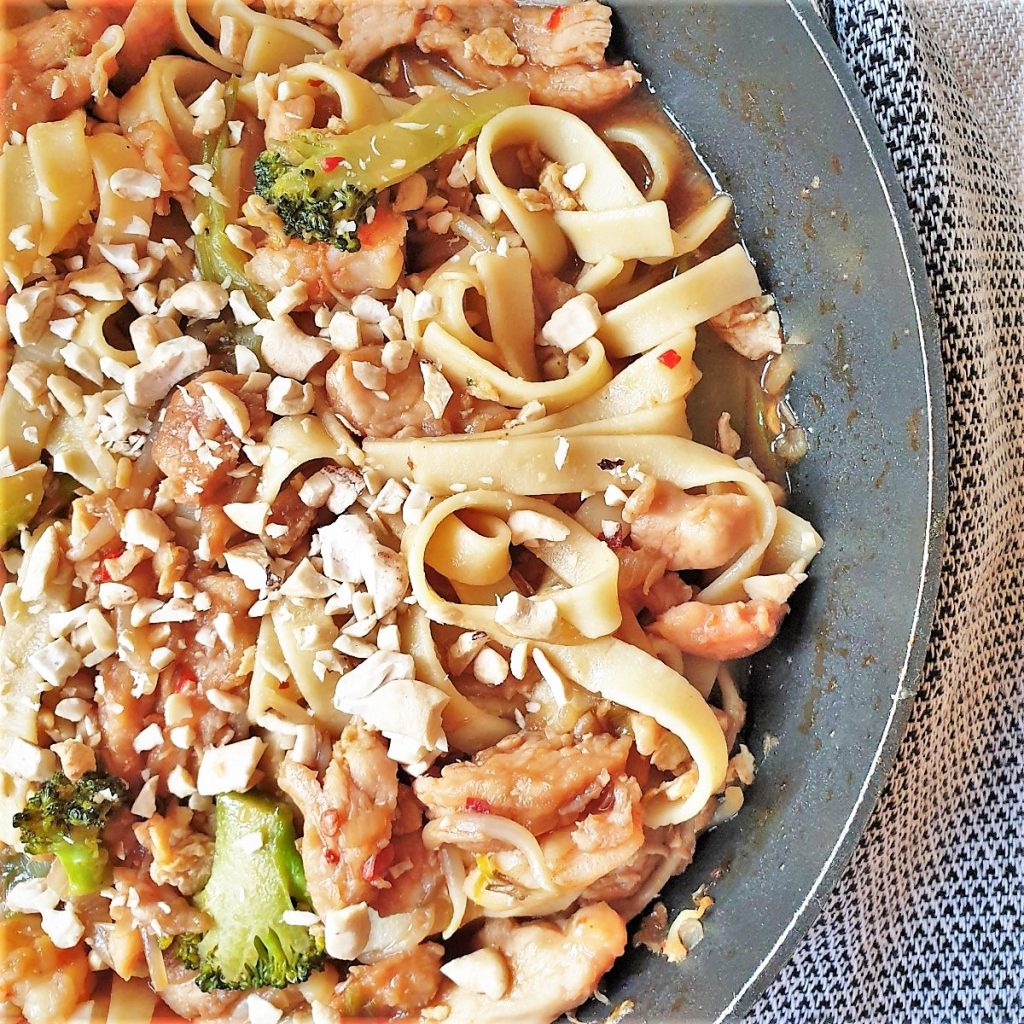 A pan of chicken and shrip pad thai noodles garnished with peanuts.