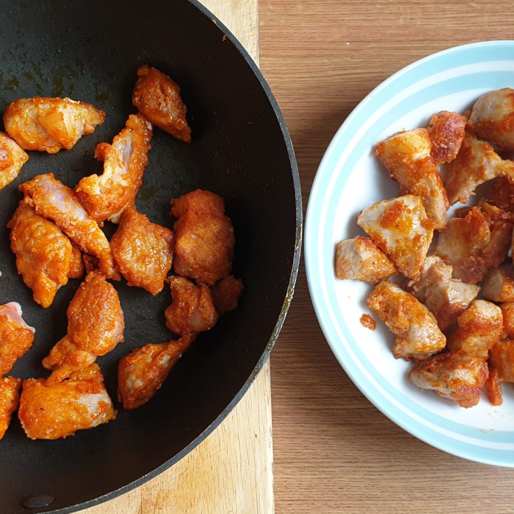 Pork pieces being browned in a frying pan.