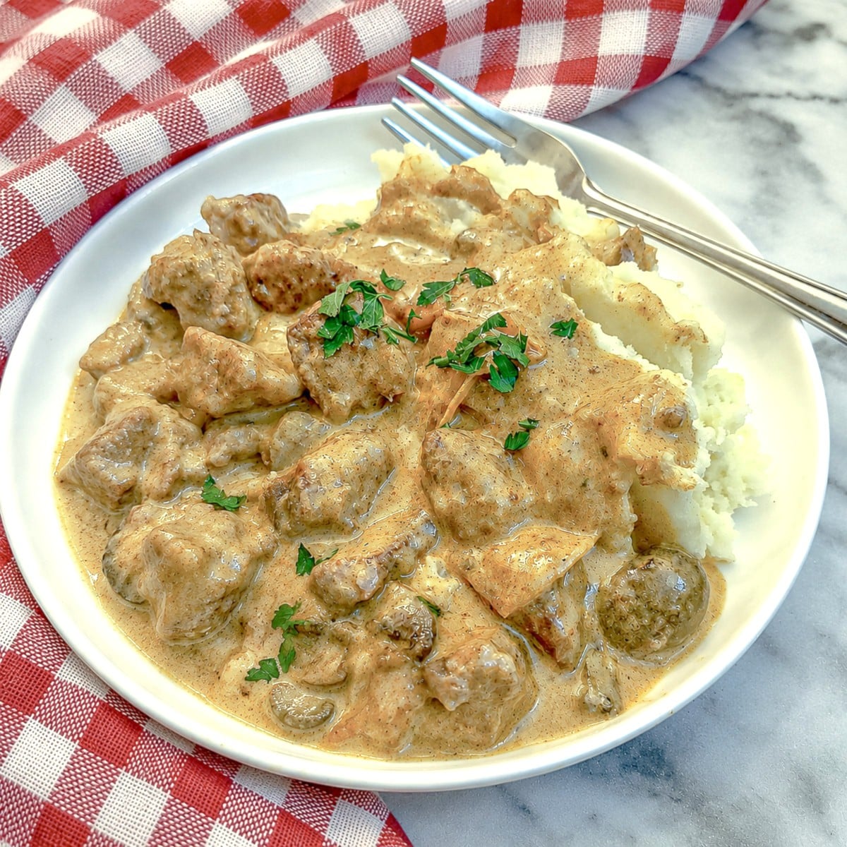Closeup of a plate of paprika pork spooned over a bed of mashed potatoes.