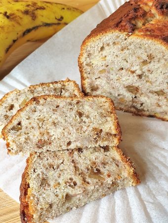 Slices of banana walnut bread in front of the whole loaf, next to a banana.