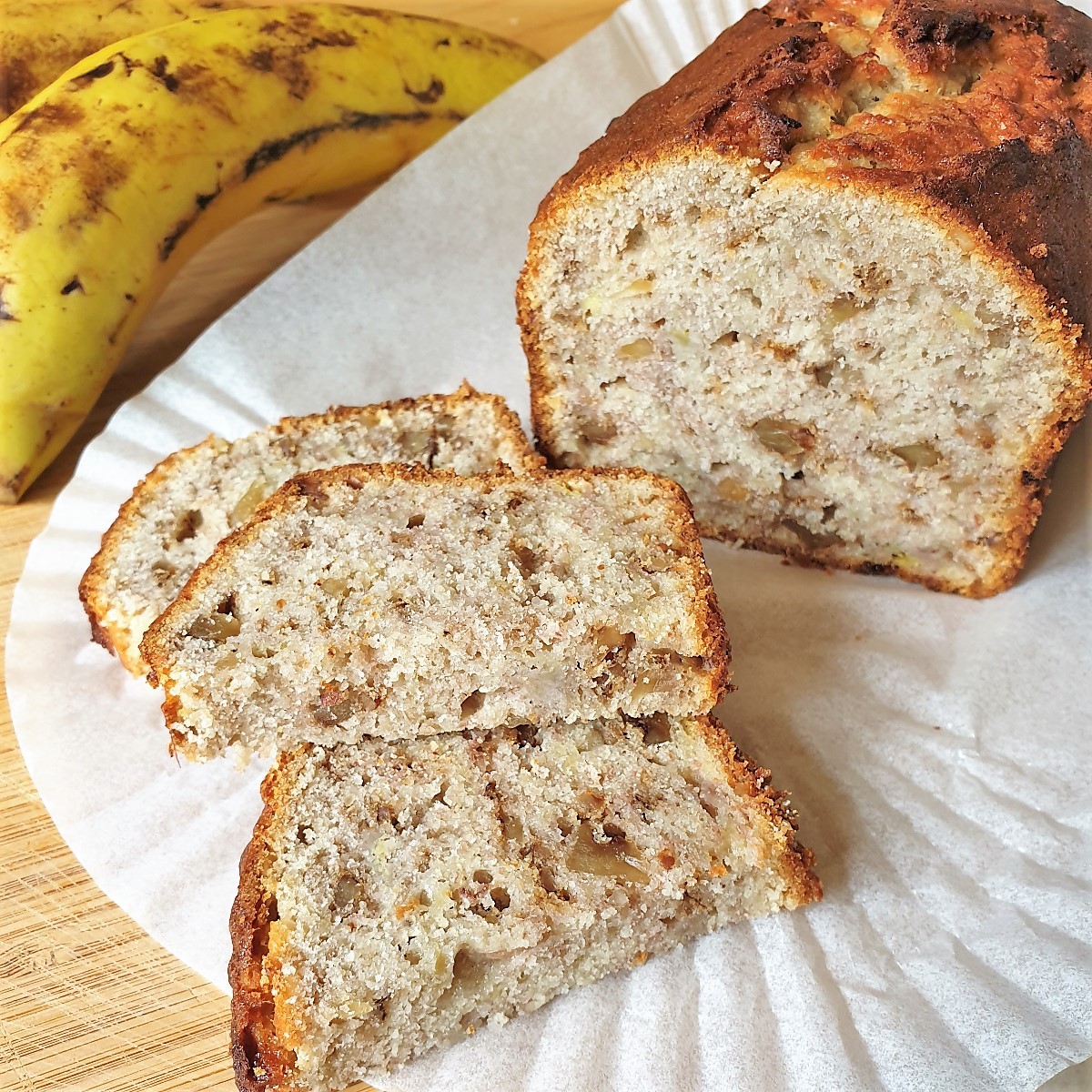 Slices of banana walnut bread in front of the whole loaf, next to a banana.