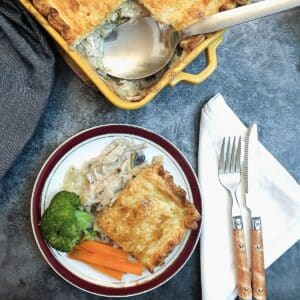 A slice of chicken, leek and mushroom pie on a plate with vegetables.