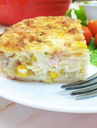 A slice of crustless ham, cheese and sweetcorn quiche on a plate with a fork.