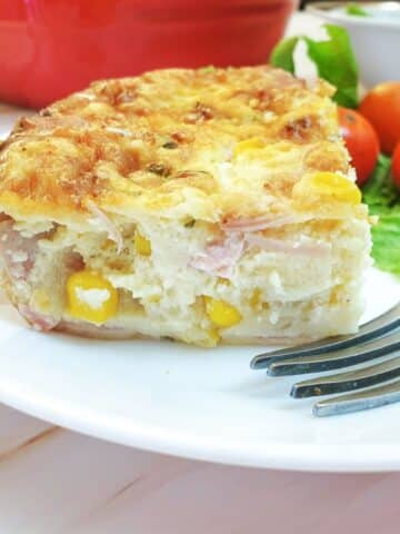 A slice of crustless ham, cheese and sweetcorn quiche on a plate with a fork.