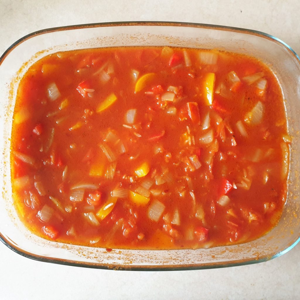 Tomatoes, onions and peppers in a dish of sauce.