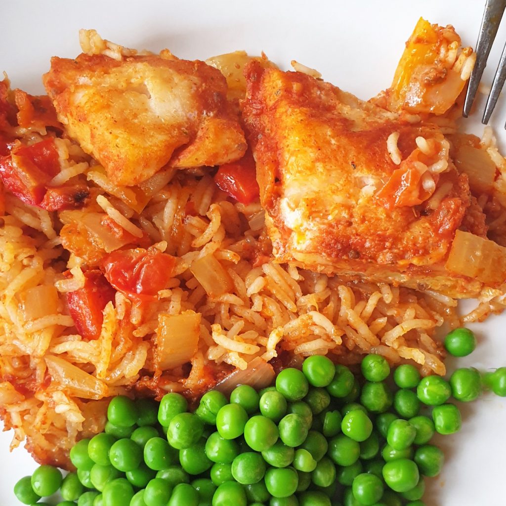 A plate of spicy fish and rice with peas.