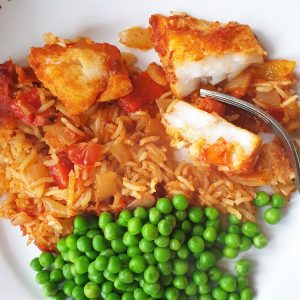 A plate of spicy fish and rice with peas.