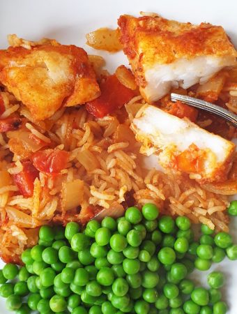 A plate of spicy fish and rice with peas.