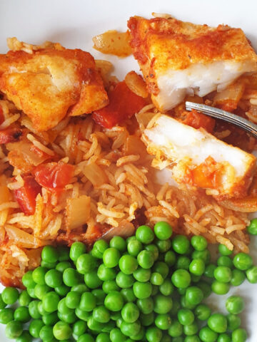 A plate of spicy fish and rice with peas.