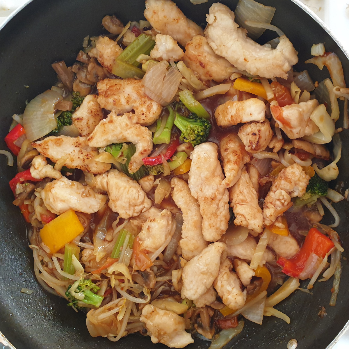 Pieces of garlic chicken being stir fried in a pan with vegetables..