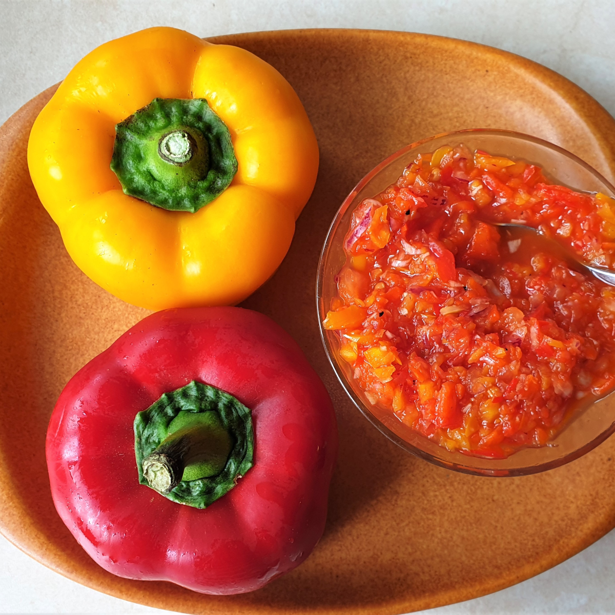 A red pepper and yellow pepper along side a dish of sweet pepper relish.