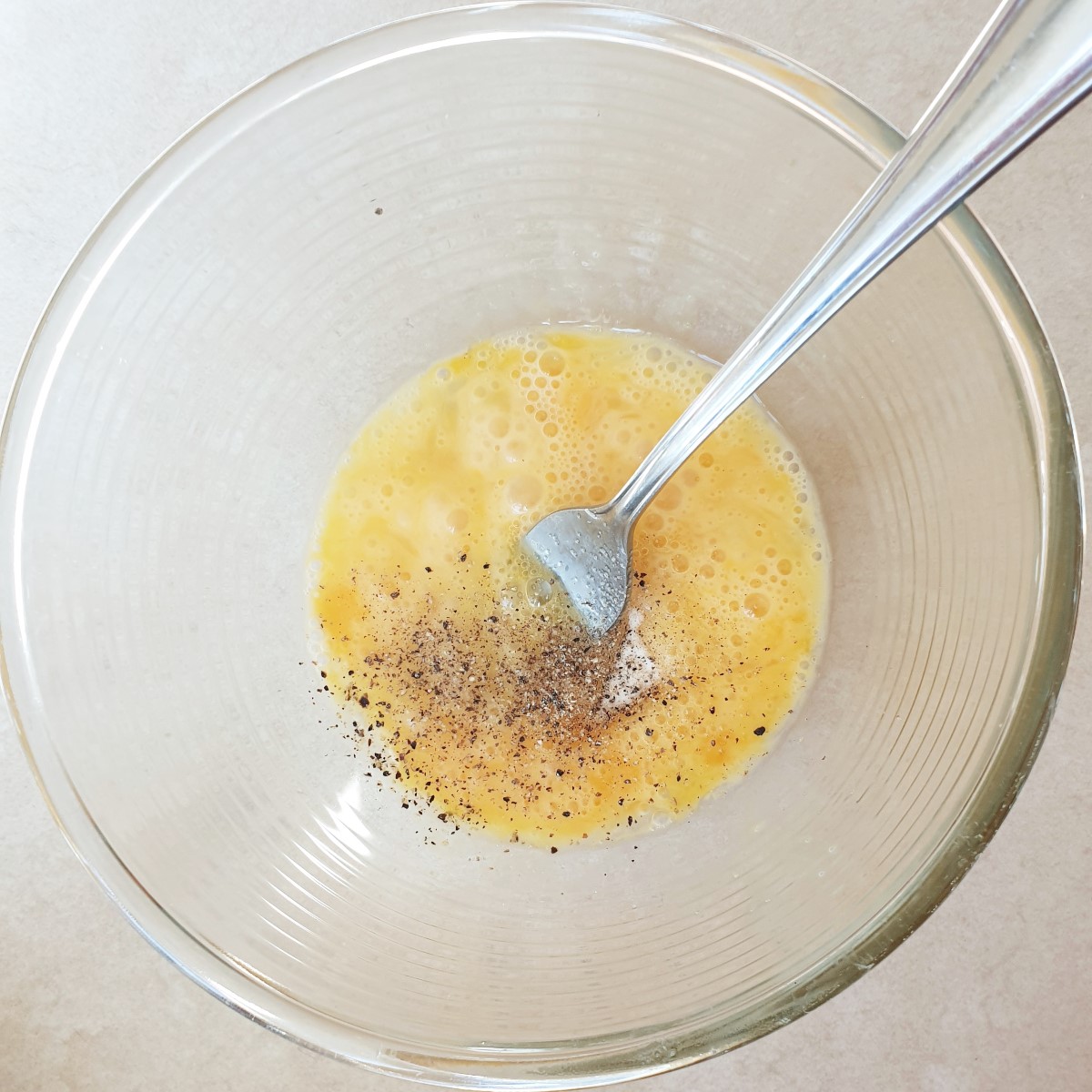 A bowl of beaten egg and flour with black pepper being added.