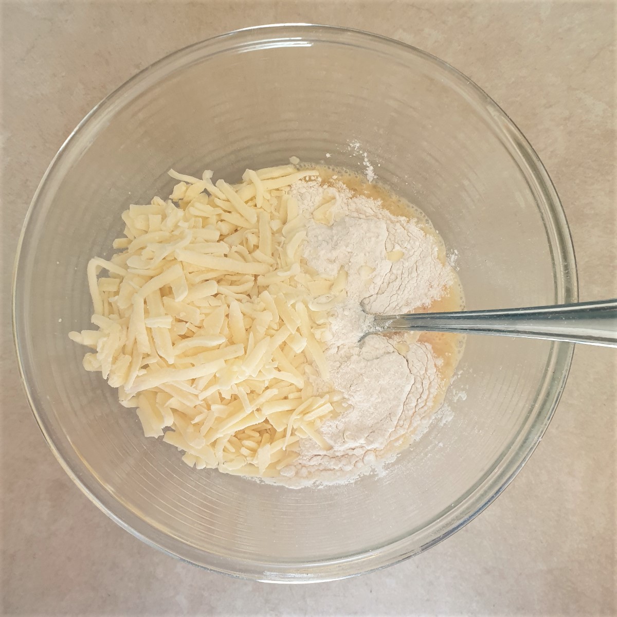 A bowl of sweetcorn batter with cheese being added.