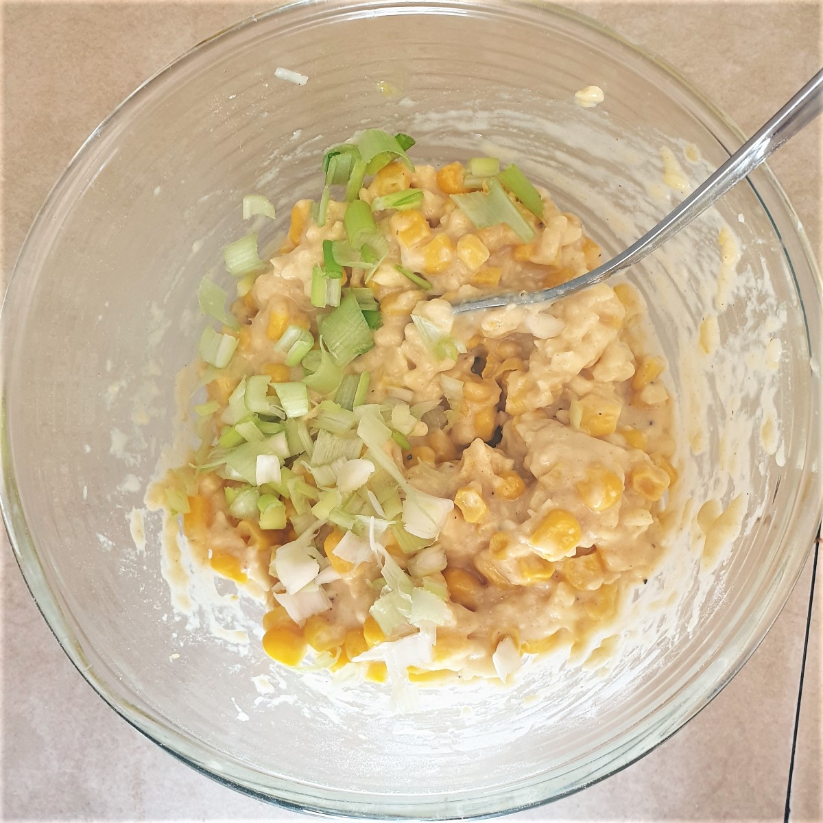 A bowl of sweetcorn and cheese batter with spring onions being added.