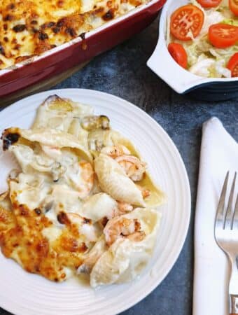 A plate of seafood stuffed pasta shells covered in cheese sauce.