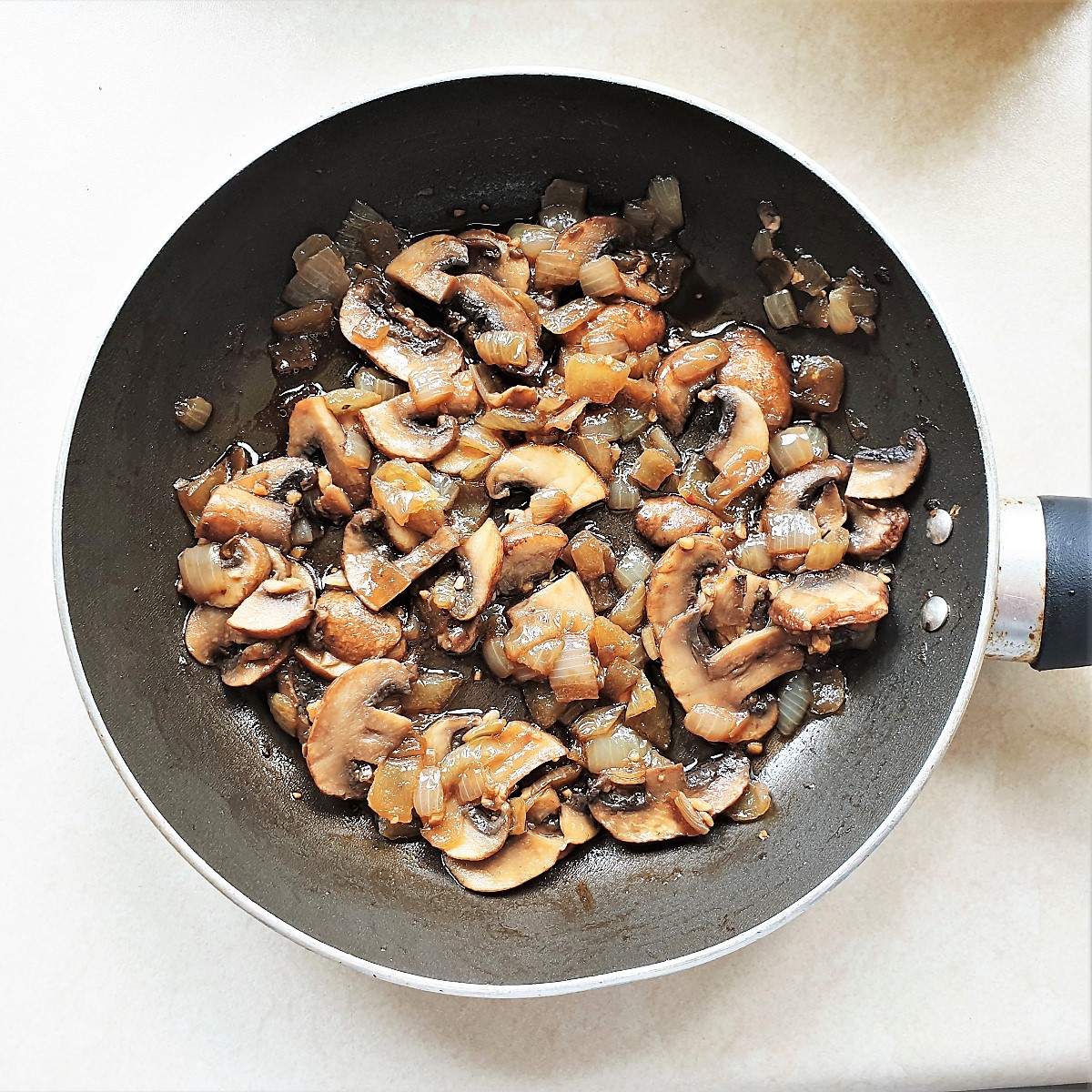 Mushrooms and onions frying in a pan.