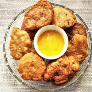 A plate of banana fritters surrounding a bowl of lemon caramel dipping sauce.