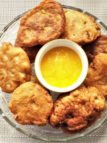 A plate of banana fritters surrounding a bowl of lemon caramel dipping sauce.