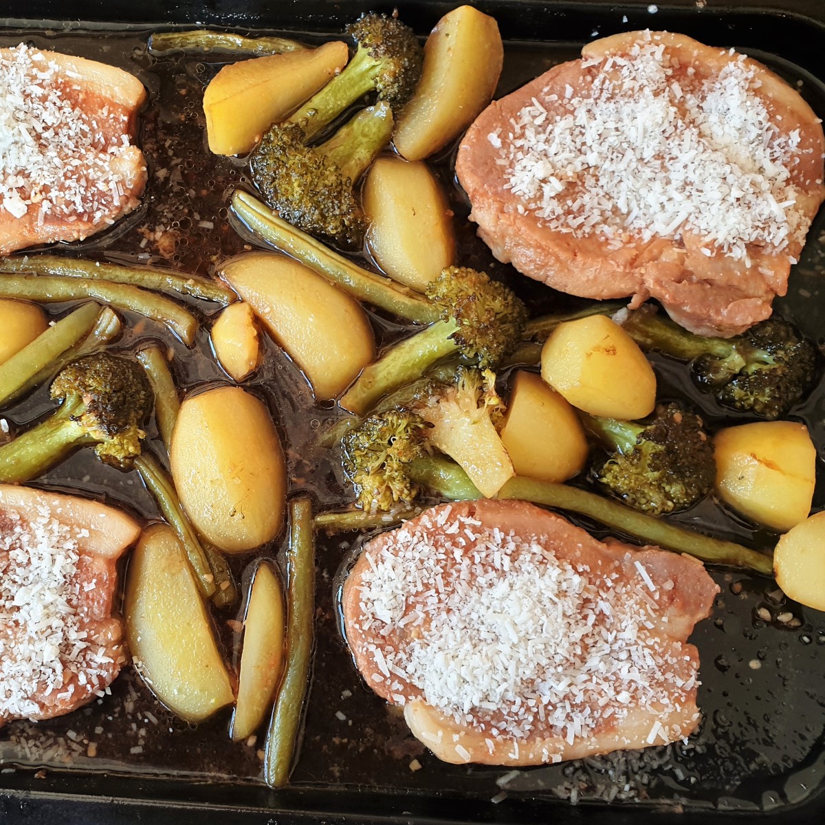 Sheet pan port chops with potatoes, broccoli and green beans sprinkled with parmesan.
