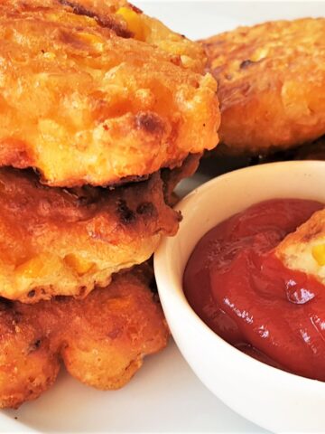 A pile of three fried crispy sweetcorn fritters with a dipping sauce.