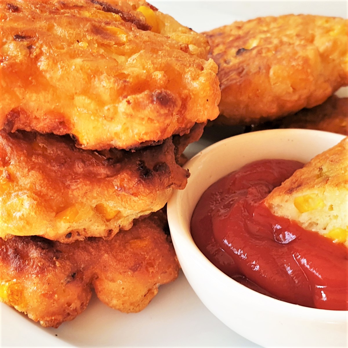 A pile of three fried crispy sweetcorn fritters with a dipping sauce.