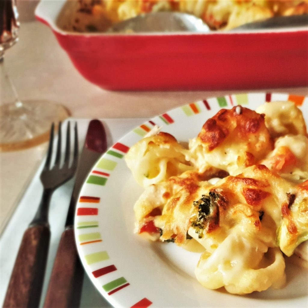 A plate of chicken and vegetable pasta bake next to the baking dish.