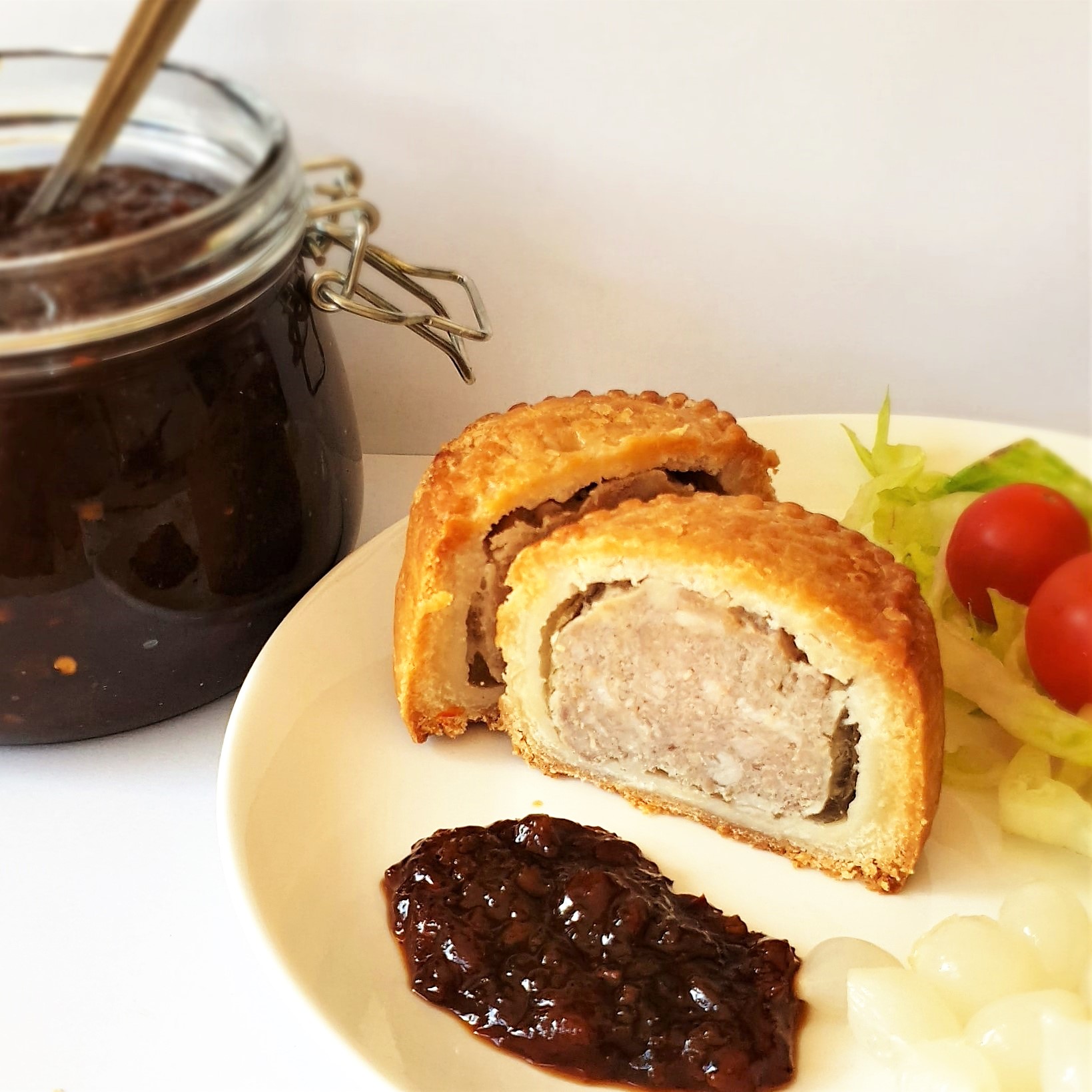 A slice of pork pie on a plate alongside a spoonful of Mrs Balls chutney.