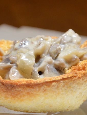 A single breadcup filled with creamed mushrooms on a plate.