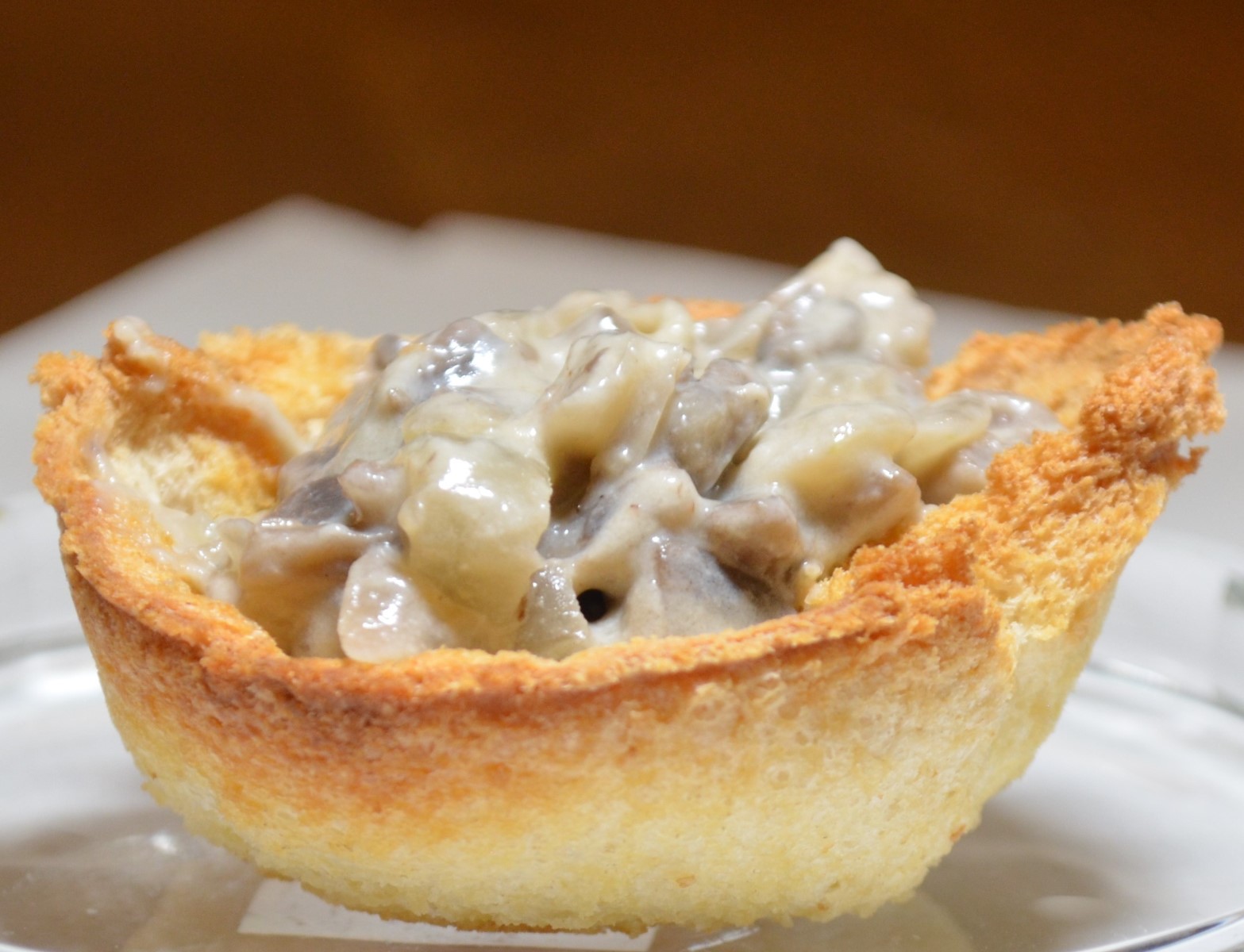 A single breadcup filled with creamed mushrooms on a plate.