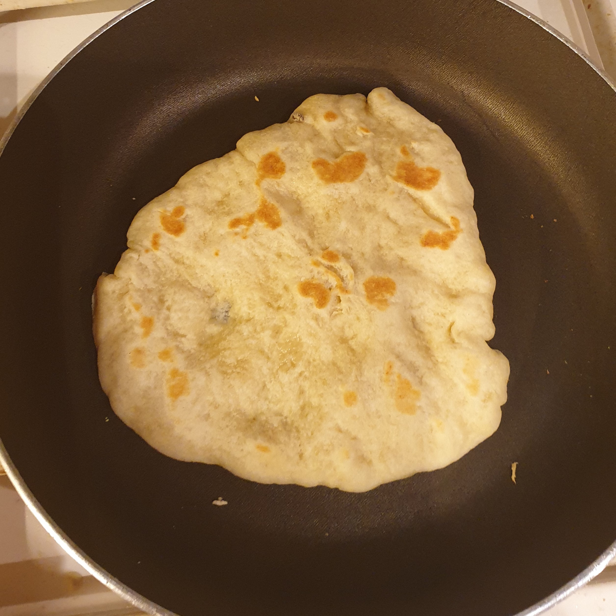 Homemade naan bread in a frying pan.