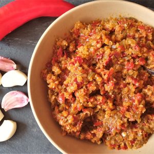 A bowl of jalapeno chili past with a red chili and cloves of garlic.