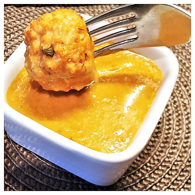 A Thai meatball on a fork being dipped in a bowl of homemade satay sauce.