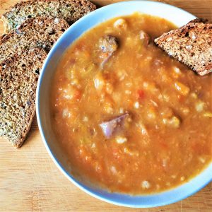 A dish of beef vegetable soup with a slice of bread.