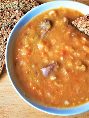 A dish of beef vegetable soup with a slice of bread.