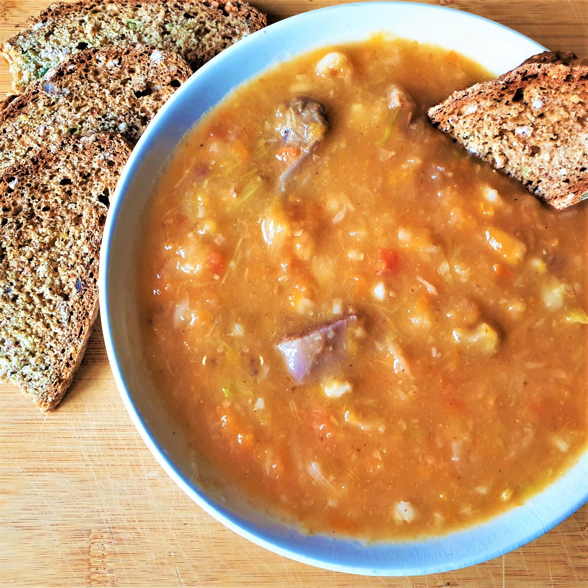 A bowl of beef vegetable soup with slices of bread.