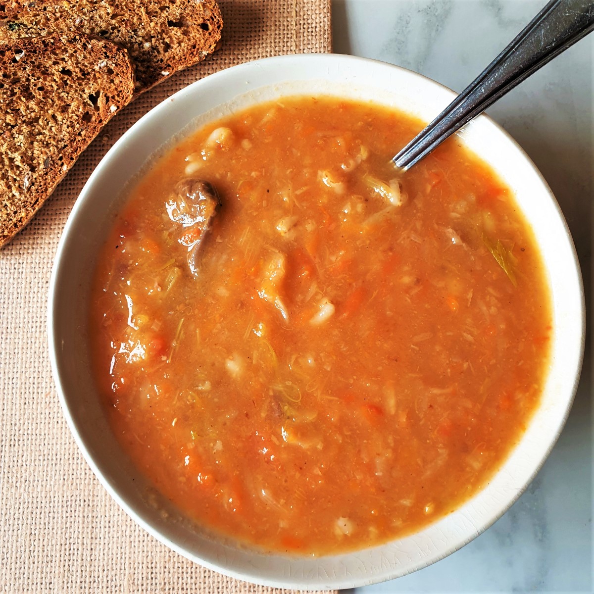 A  bowl of beef vegetable soup with a slice of brown crusty bread.