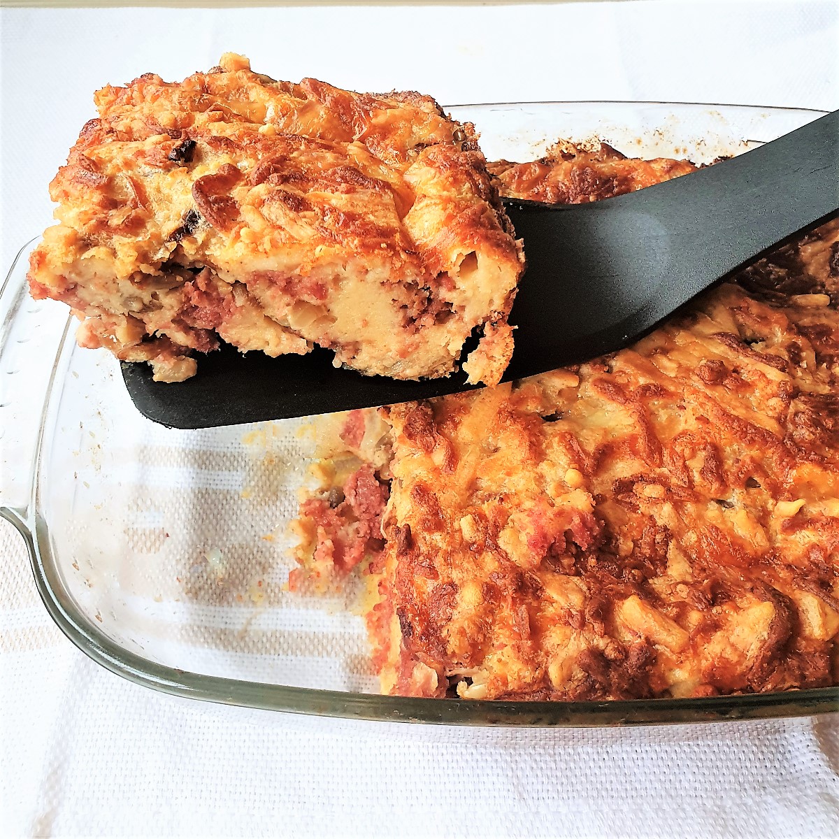 A slice of bully beef quiche being lifted from the baking dish.