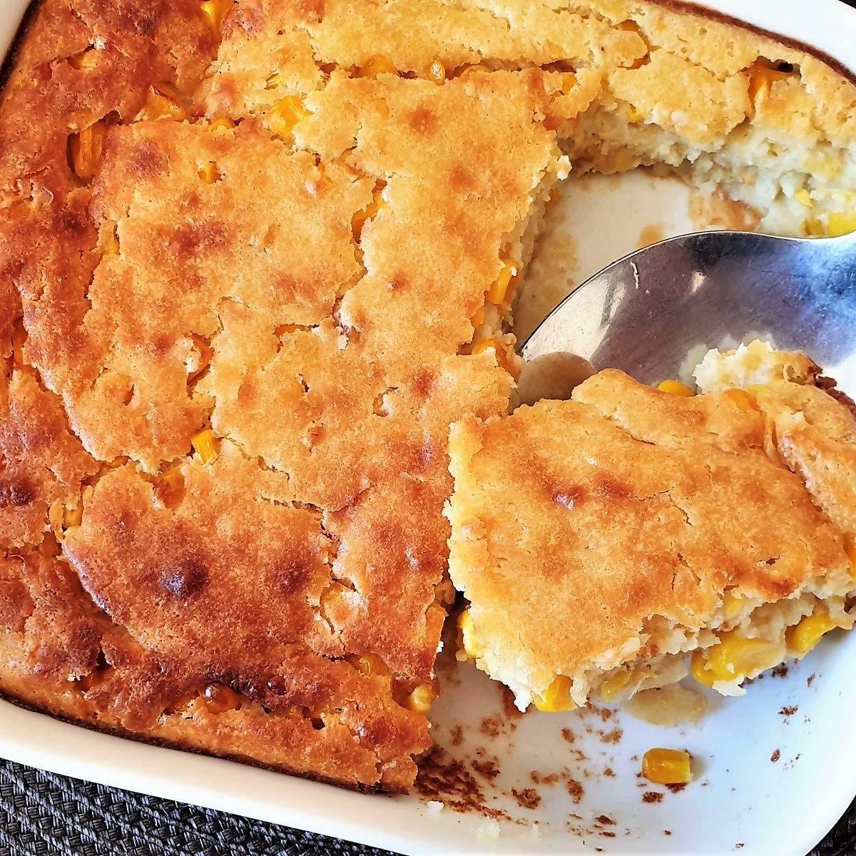 A spoonful of cornbread casserole being lifted from the baking dish.