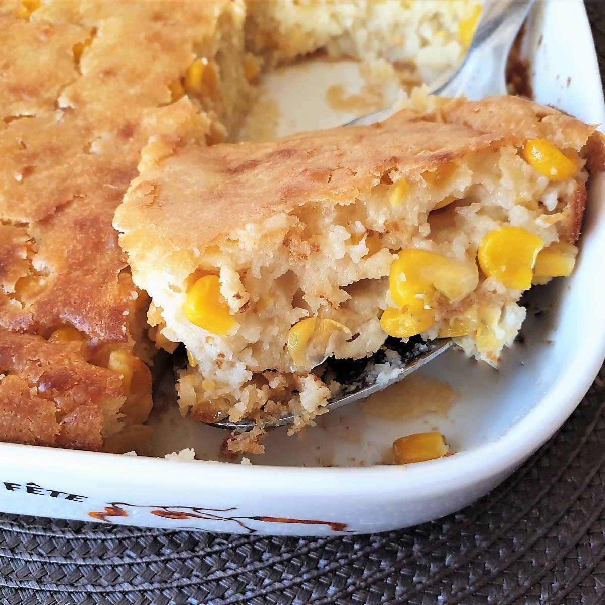 A spoonful of cornbread casserole being lifted from the baking dish.