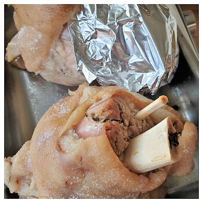 Cooked pork knuckles partially covered with tinfoil before being crisped.