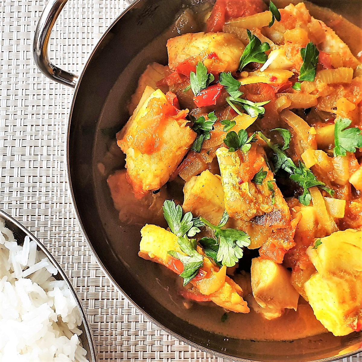 Fish curry in a balti dish next to a dish of white rice.