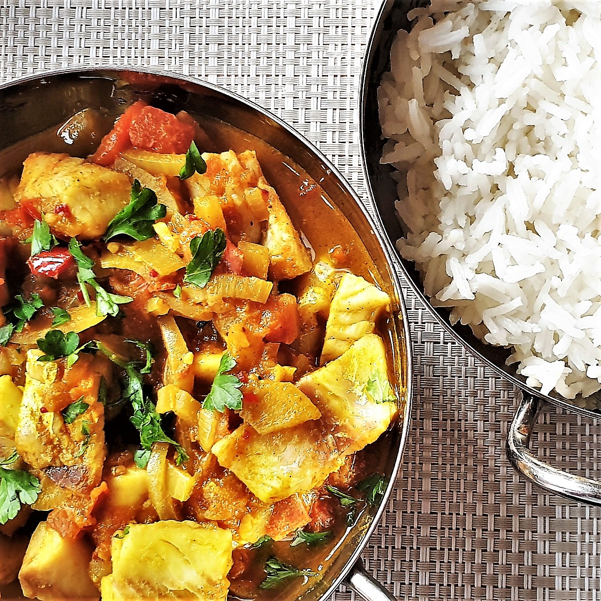 A bowl of fish curry next to a bowl of white rice.