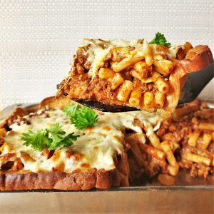 A slice of garlic bread pasta bake being lifted from the dish.