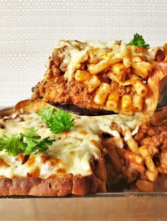 A slice of garlic bread pasta bake being lifted from the dish.