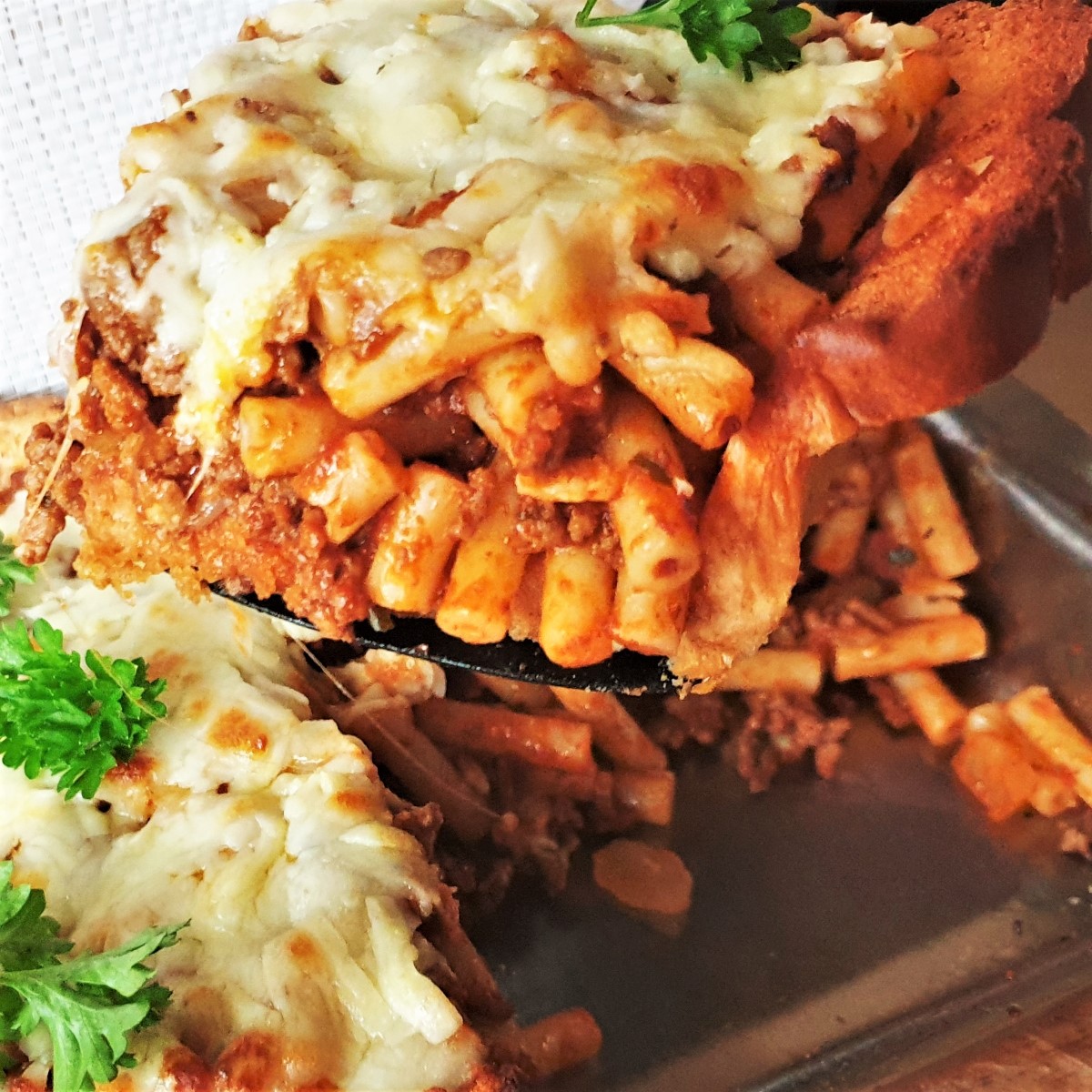 A slice of garlic bread pasta bake being lifted from a dish.